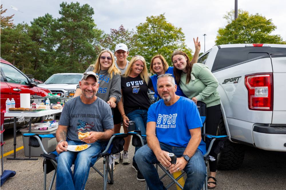 Attendees pose for a picture near truck in tailgate parking lot.